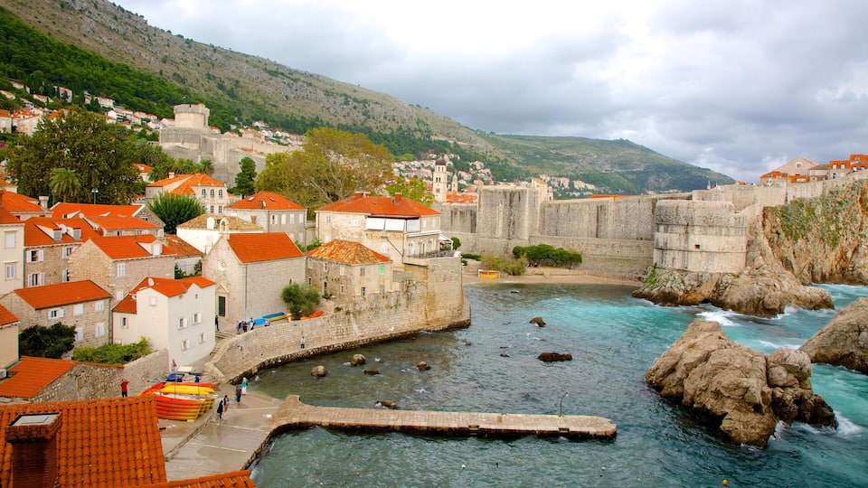 Un poble costaner amb edificis de pedra històrics, una muralla fortificada i un mar blau clar.