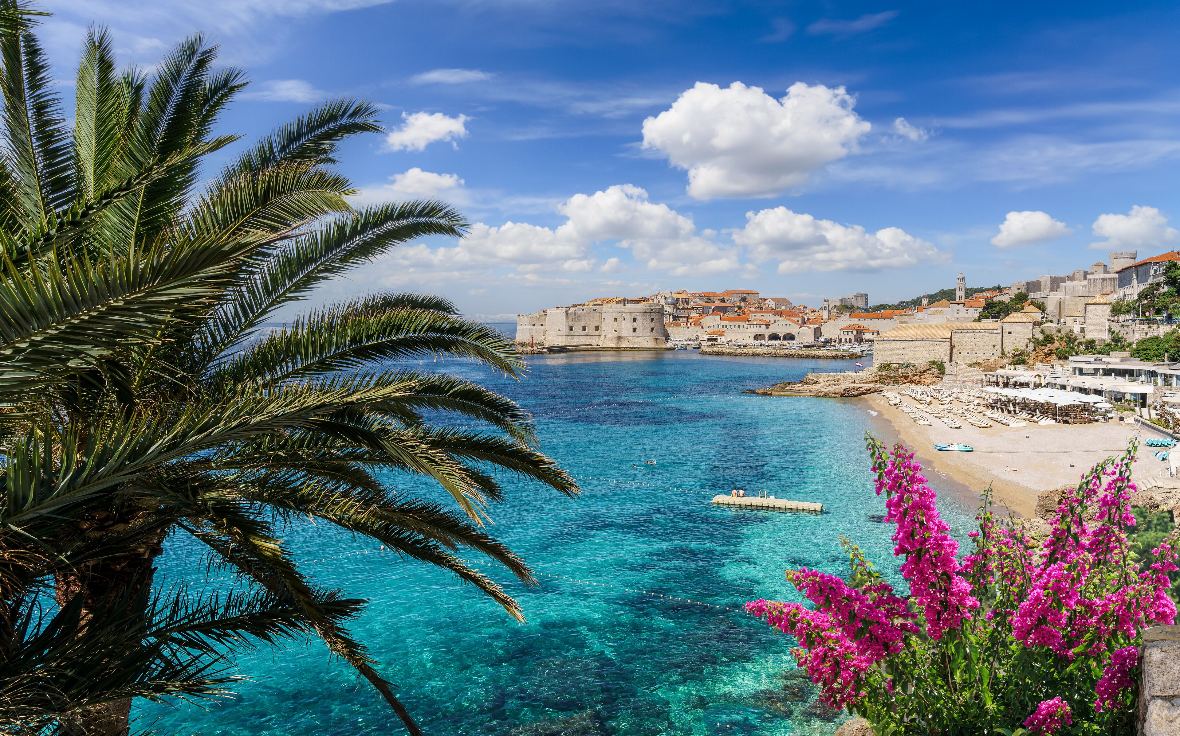 Un pueblo costero con aguas azul turquesa, una fortaleza histórica y una playa con sillas de descanso.