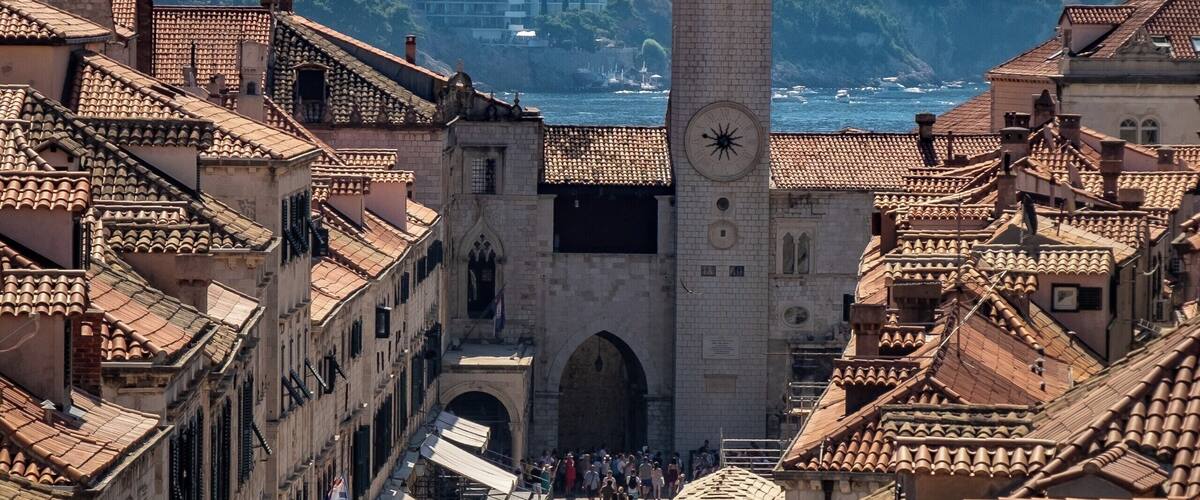 Una plaza animada con una imponente torre del reloj, rodeada de edificios históricos con tejados de teja.