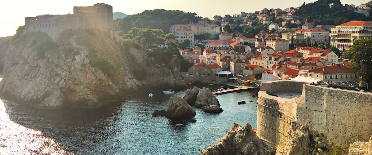 A coastal town with a historic fortification, a harbor with boats, and a densely built urban area with red-roofed buildings.