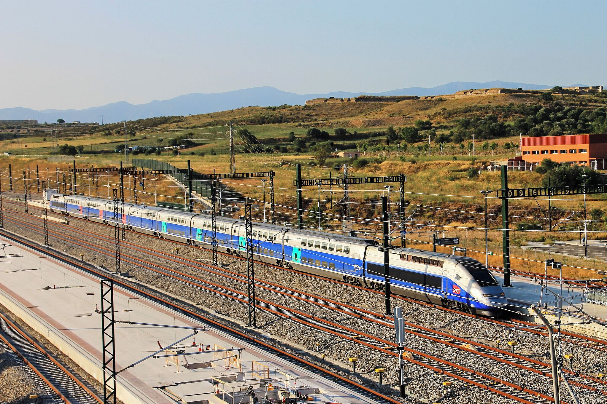 A high-speed train on multiple tracks with a mountainous landscape in the background.