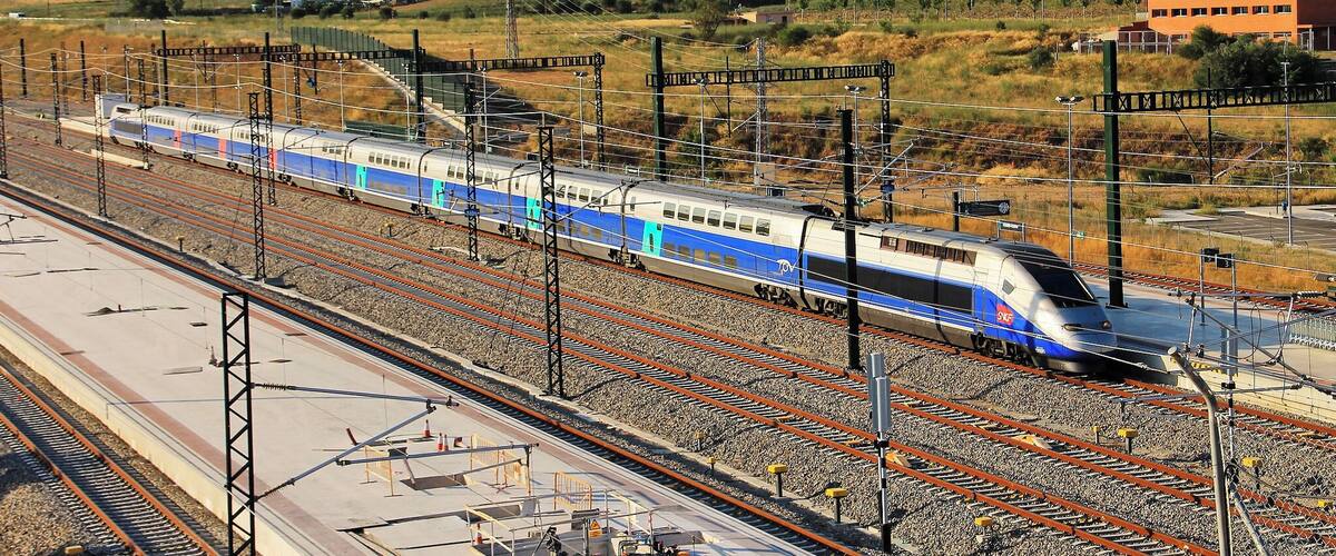 A high-speed train on multiple tracks with a mountainous landscape in the background.