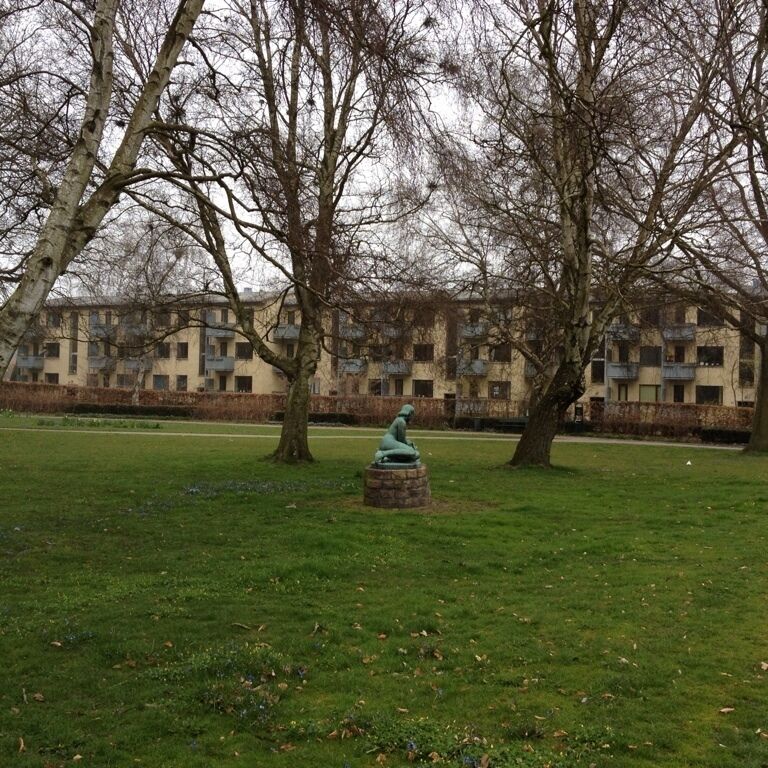 A park with a statue, trees, and a building in the background.
