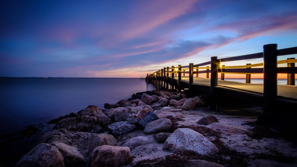 A pier extending into calm waters at dusk with a colorful sky.