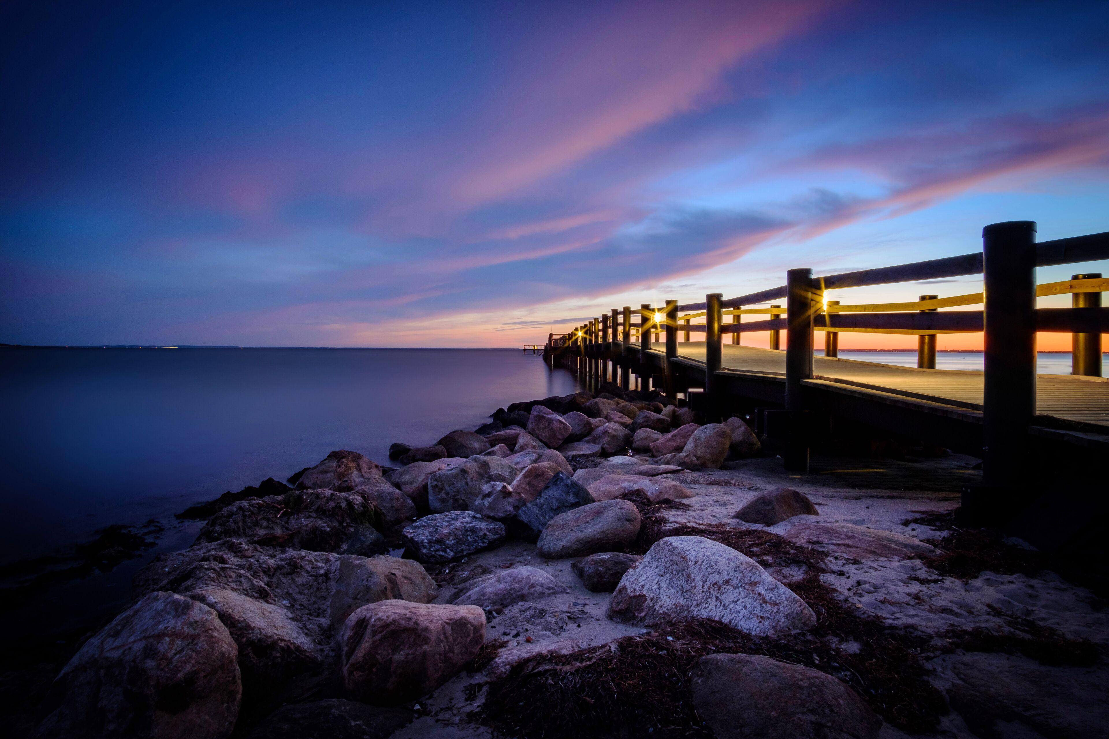 A pier extending into calm waters at dusk with a colorful sky.