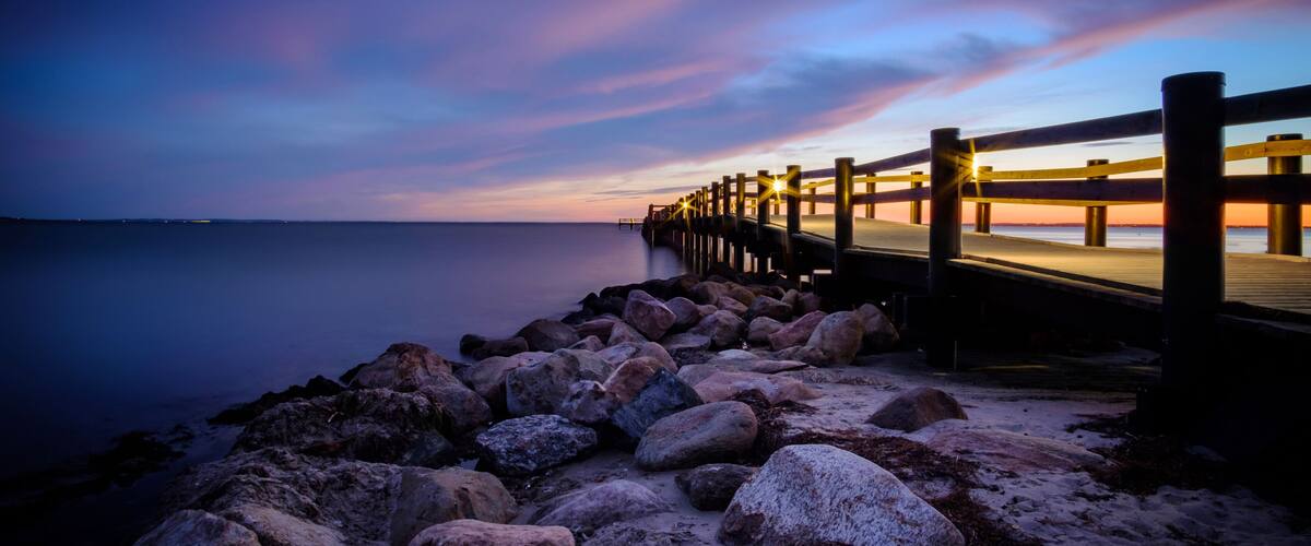 A pier extending into calm waters at dusk with a colorful sky.