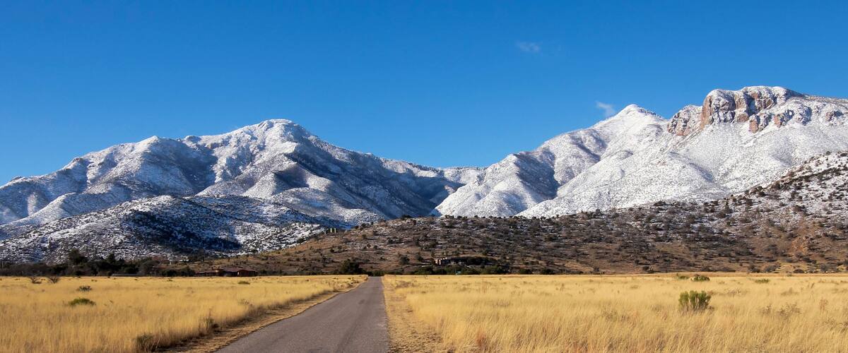A road leading to snow-capped mountains with a clear blue sky.
