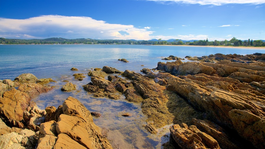 Una costa rocosa con aguas cristalinas y colinas al fondo.