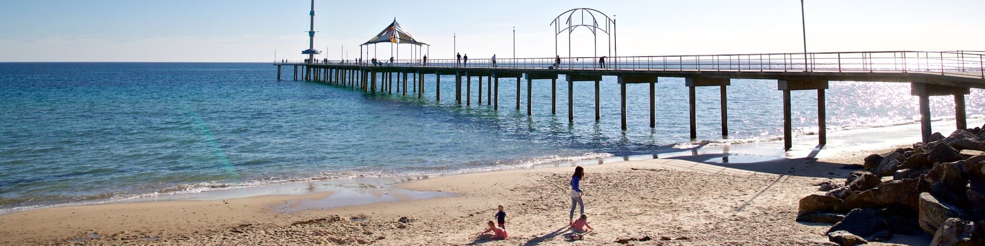 A beach with a pier extending into the ocean, a lighthouse, and a clear blue sky.