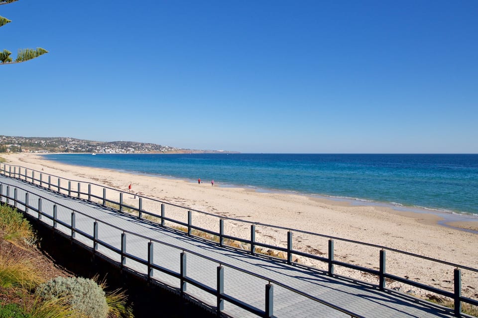 A coastal walkway leading to a sandy beach with clear blue waters.