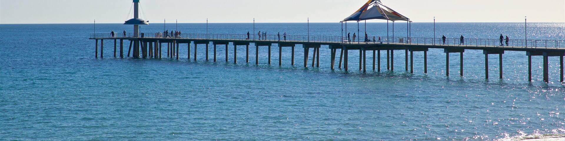 A pier extending into the sea with a lighthouse and a shaded pavilion.