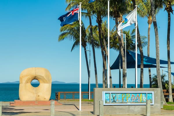 A coastal scene with a large concrete sculpture, palm trees, and flags including the Australian flag.