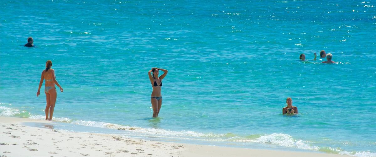 A beach with clear turquoise water and people swimming and walking along the shore.