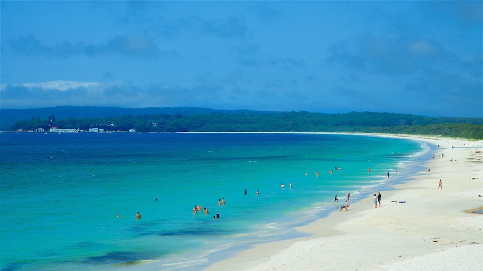 A beach with clear turquoise water, a sandy shore, and a forested island in the distance.