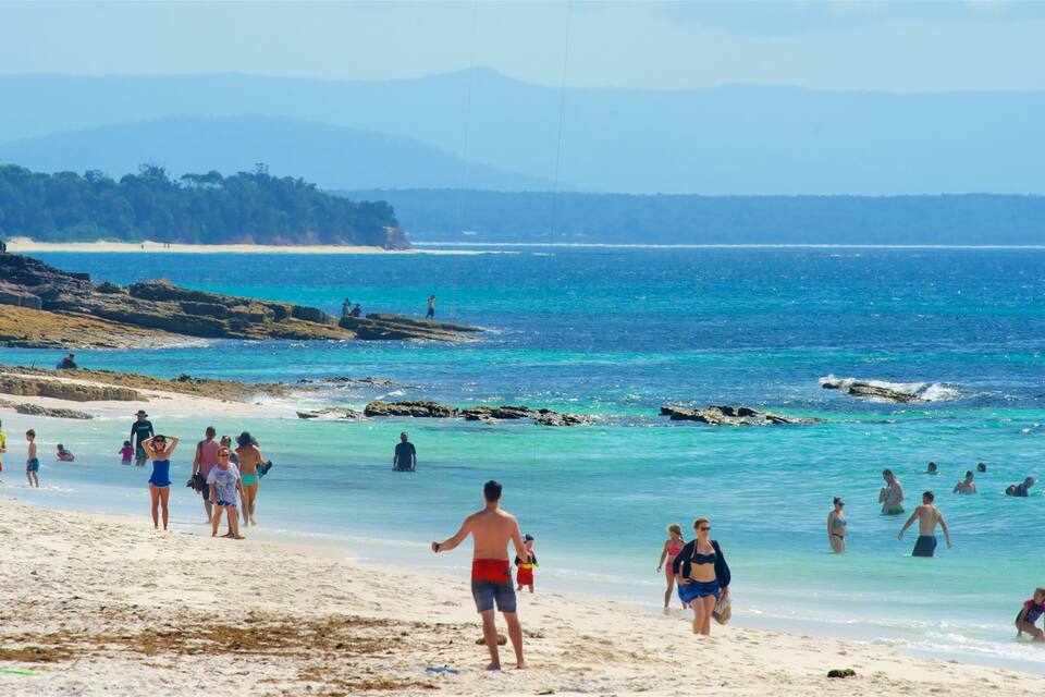 A beach with clear turquoise water, sandy shore, and rocky outcrops.