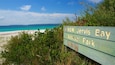 A wooden sign for NSW Jervis Bay National Park with a beach and ocean in the background.