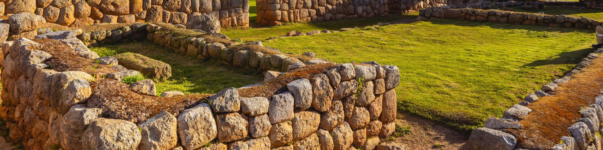 Ancient stone walls, a white church with a bell tower, and a clear blue sky with clouds.