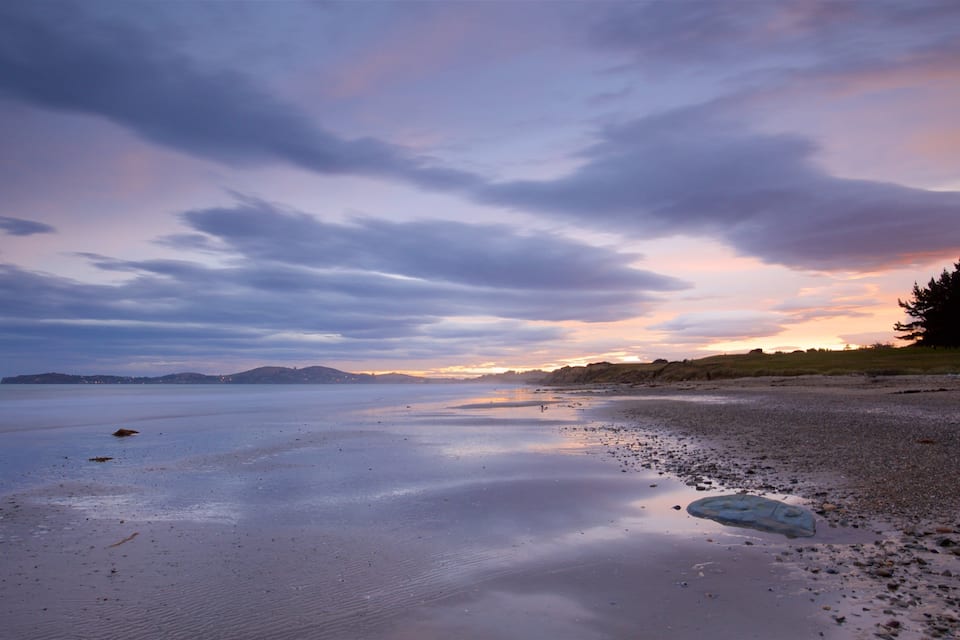 A beach with pebbles and rocks, a calm sea, and a sunset sky.