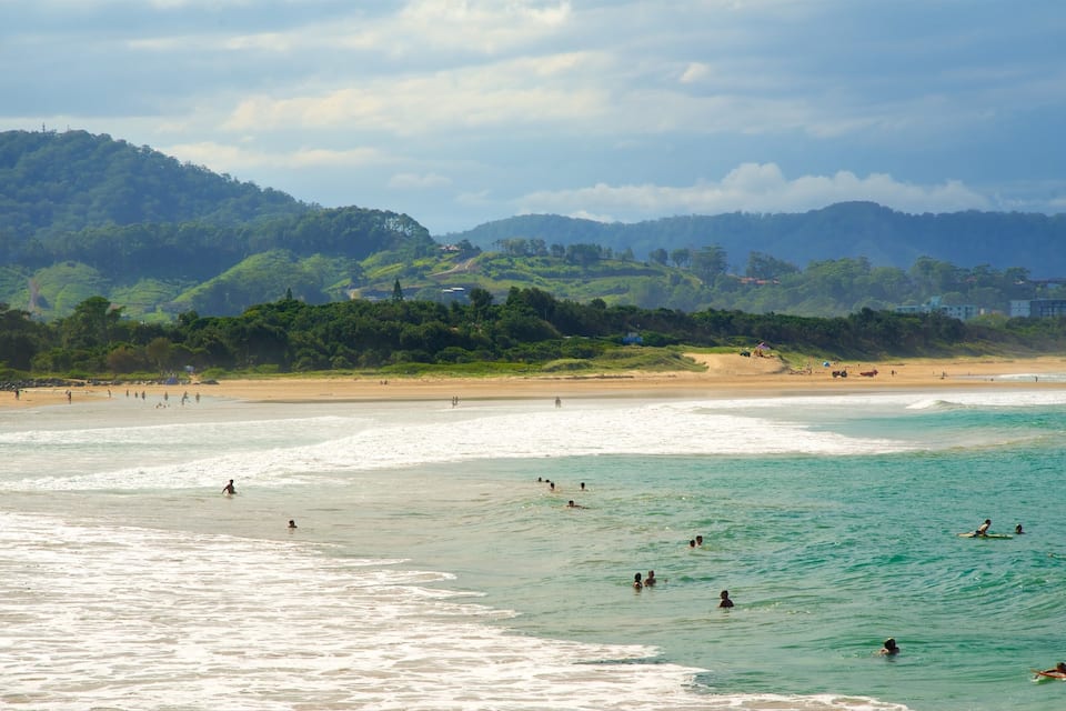 A beach with people swimming and surfing, surrounded by hills and buildings.