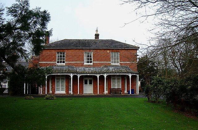 A red brick house with a white door and windows, surrounded by a green lawn and trees.
