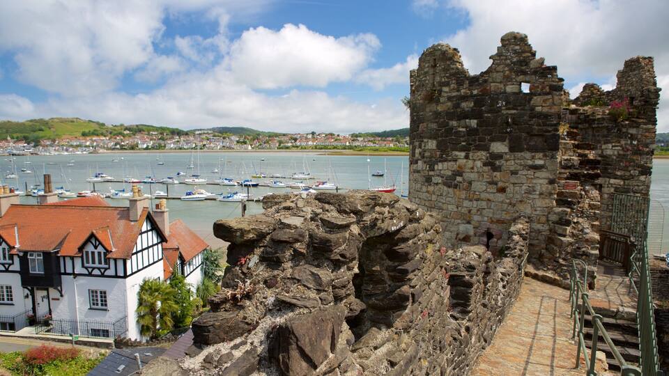 A historic stone tower and ruins by a harbor with boats.
