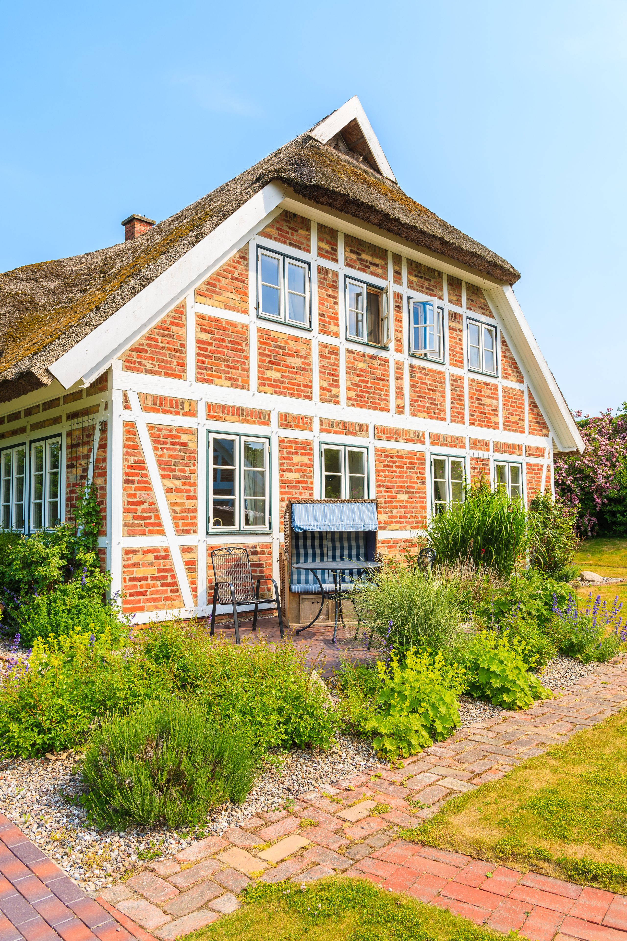Ein traditionelles Backsteinhaus mit einem Strohdach und einem Garten mit einem gepflasterten Weg.