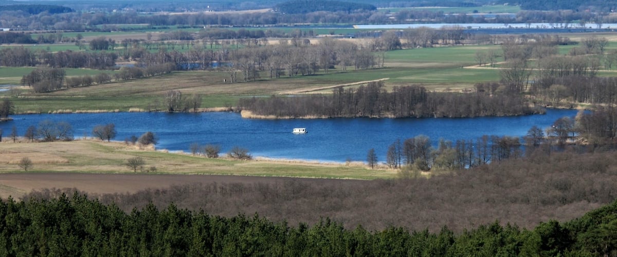 A river with a boat, surrounded by fields and forests.