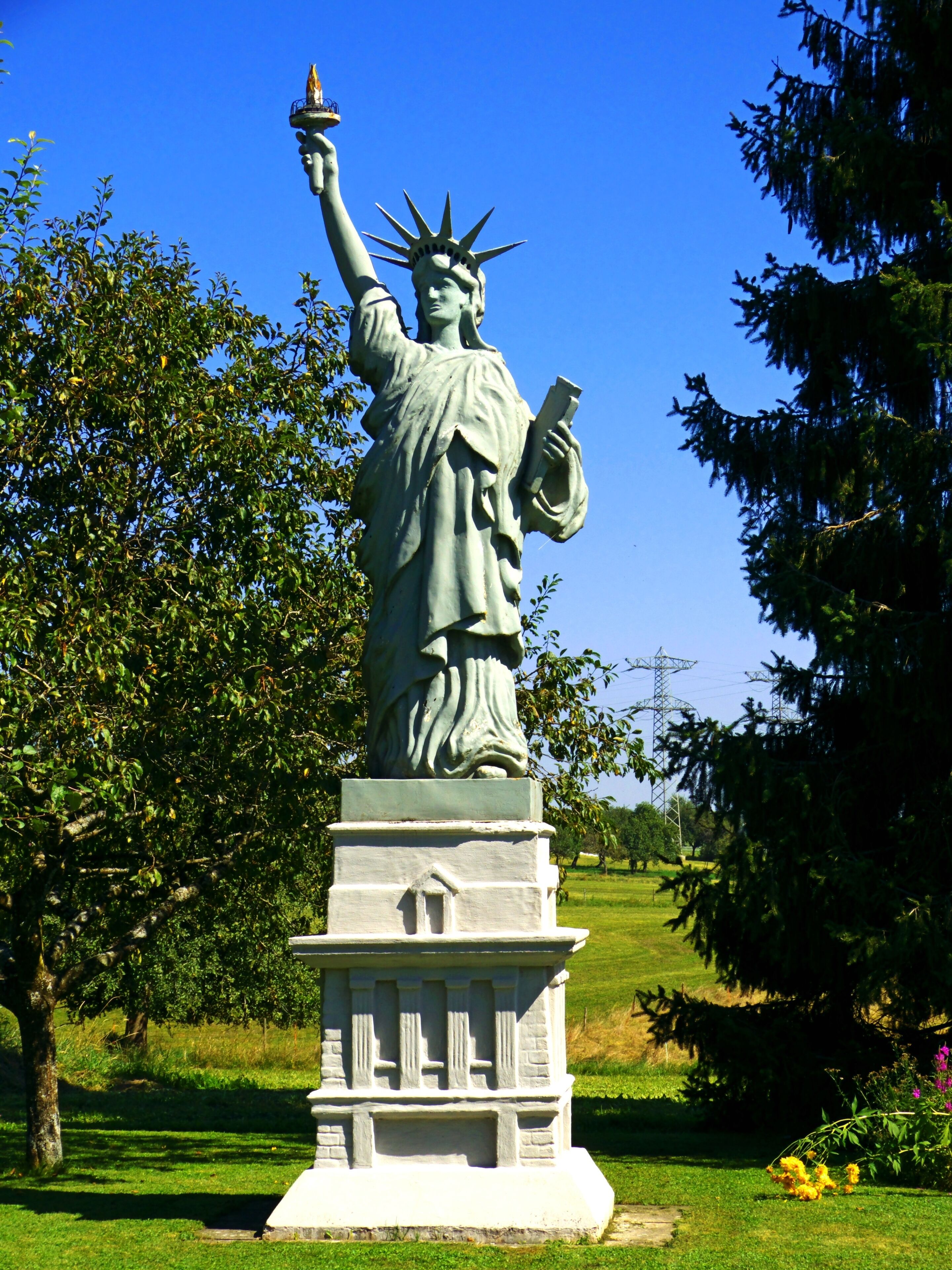 A statue of Liberty in a park with trees and grass.