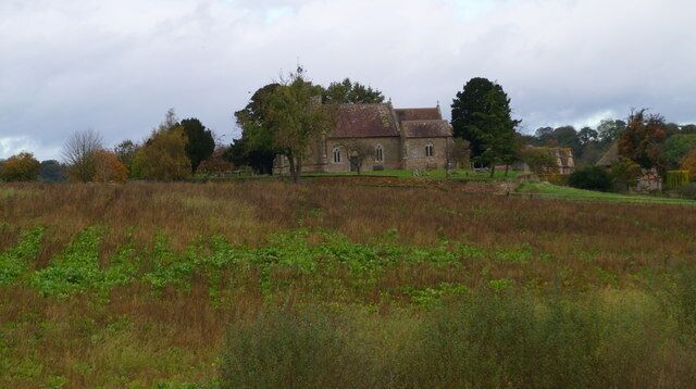 A historic stone building with a red roof, surrounded by fields and trees.