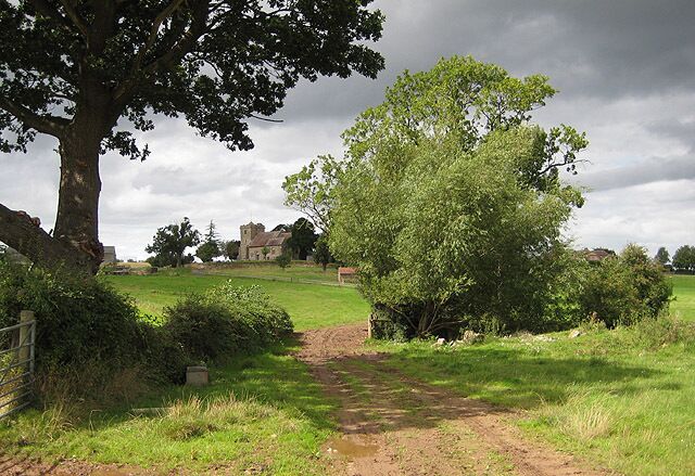 Approaching the church at Pauntley The trees on the right surround Old Mill Pond with the rooftops of Pauntley Court to their right. The church of St. John the Evangelist sits on the rise.