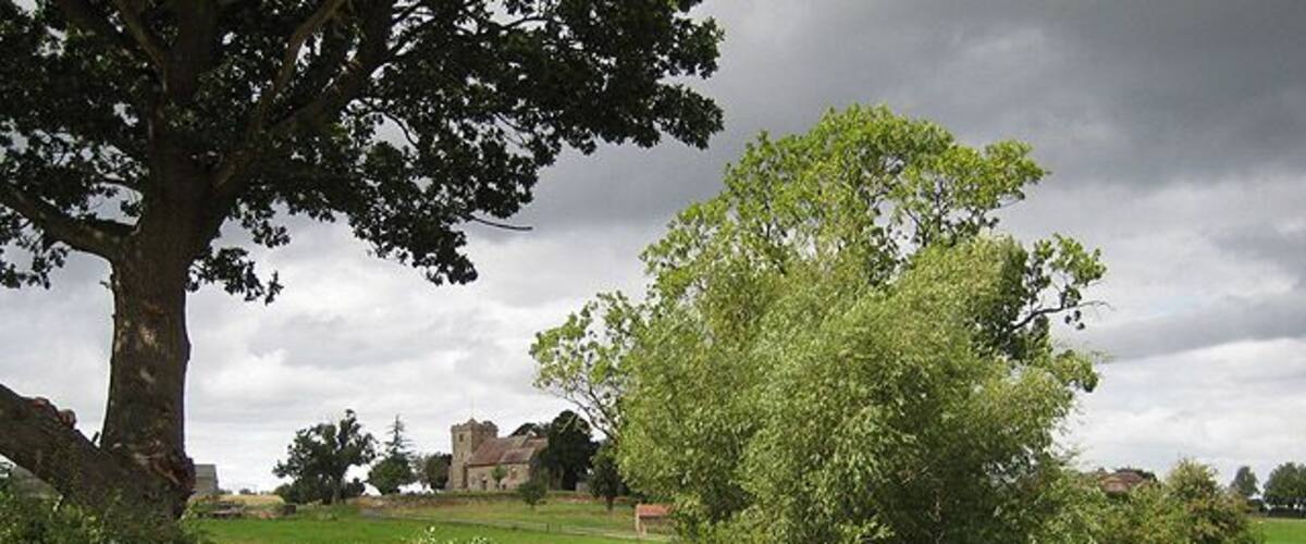 Approaching the church at Pauntley The trees on the right surround Old Mill Pond with the rooftops of Pauntley Court to their right. The church of St. John the Evangelist sits on the rise.