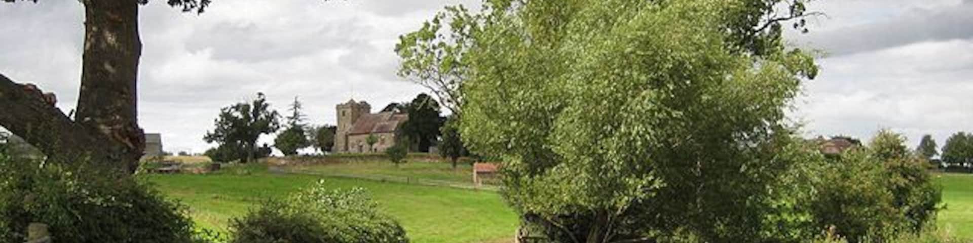 Approaching the church at Pauntley The trees on the right surround Old Mill Pond with the rooftops of Pauntley Court to their right. The church of St. John the Evangelist sits on the rise.