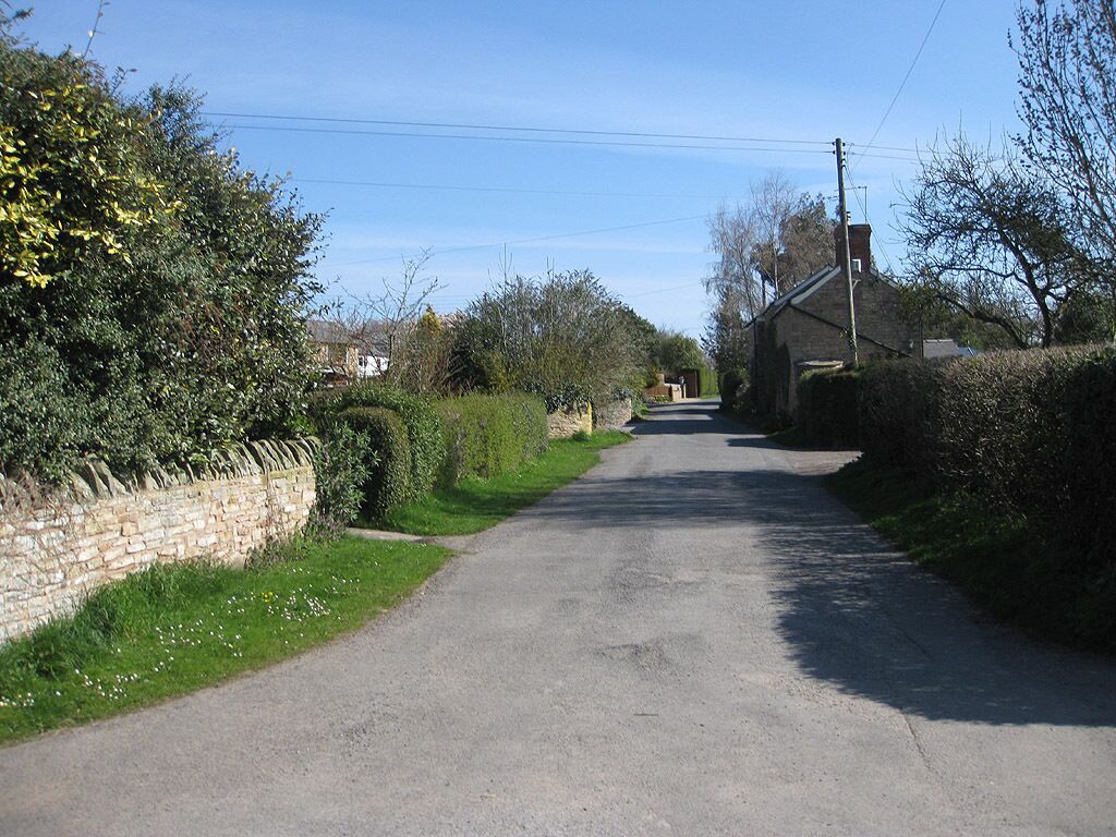 A narrow rural road flanked by stone walls and dense vegetation.
