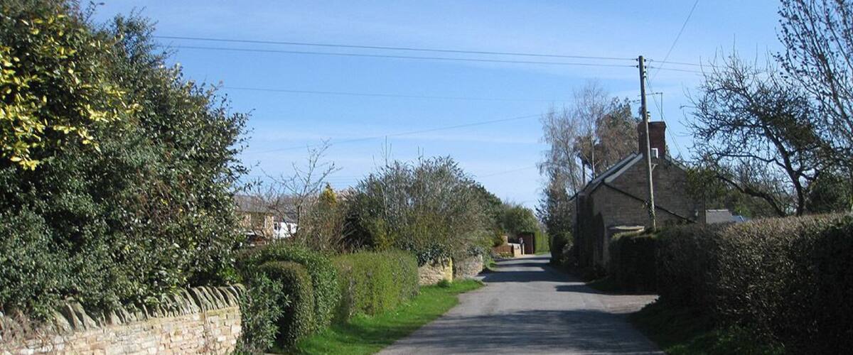 A narrow rural road flanked by stone walls and dense vegetation.