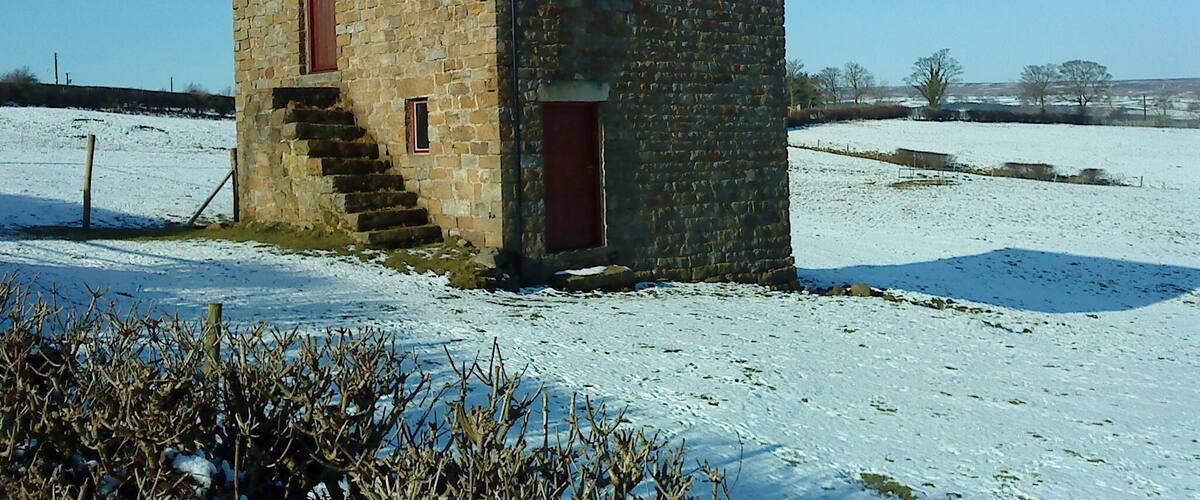 A stone building with a sloped roof in a snowy field.