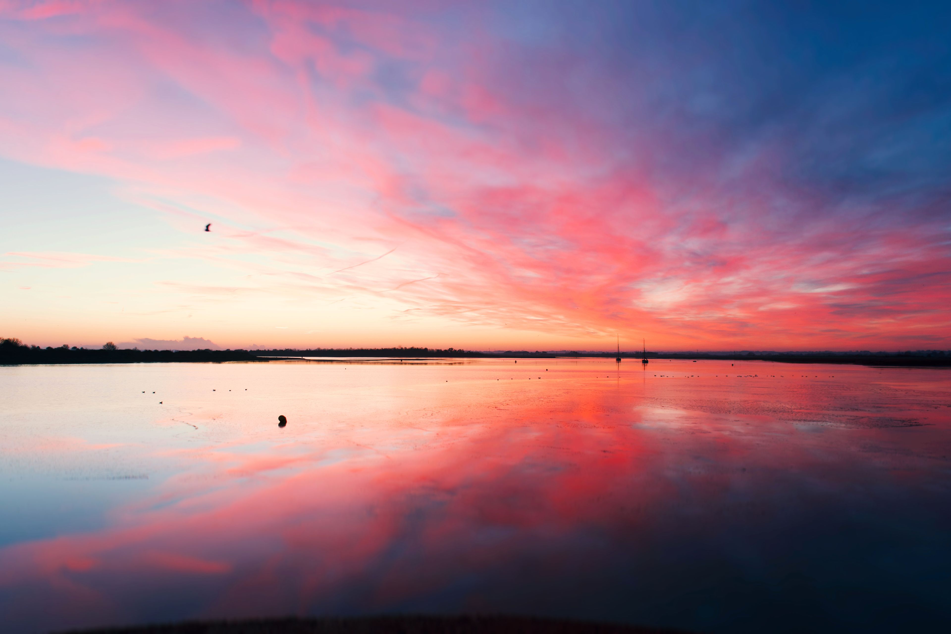 Pôr do sol sobre um lago calmo, com um céu vibrante refletido na água.