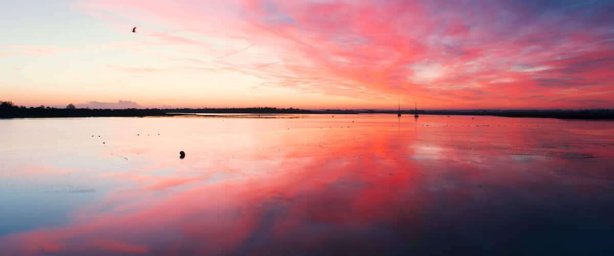 Un atardecer sobre un lago tranquilo, con un cielo vibrante reflejado en el agua.
