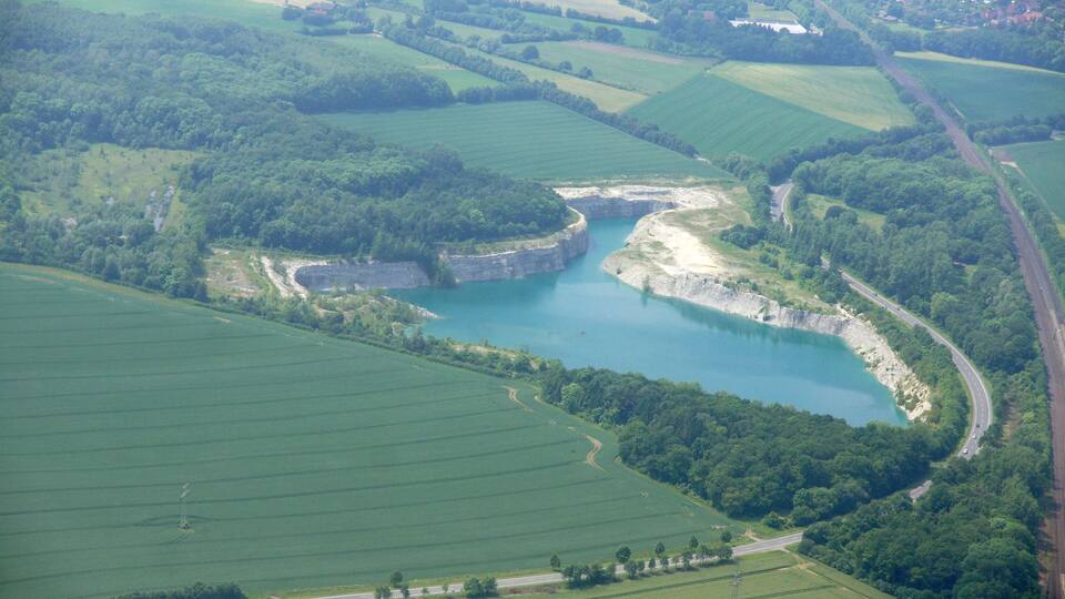 An aerial view of a green landscape with a large body of water, surrounded by fields and a winding road.