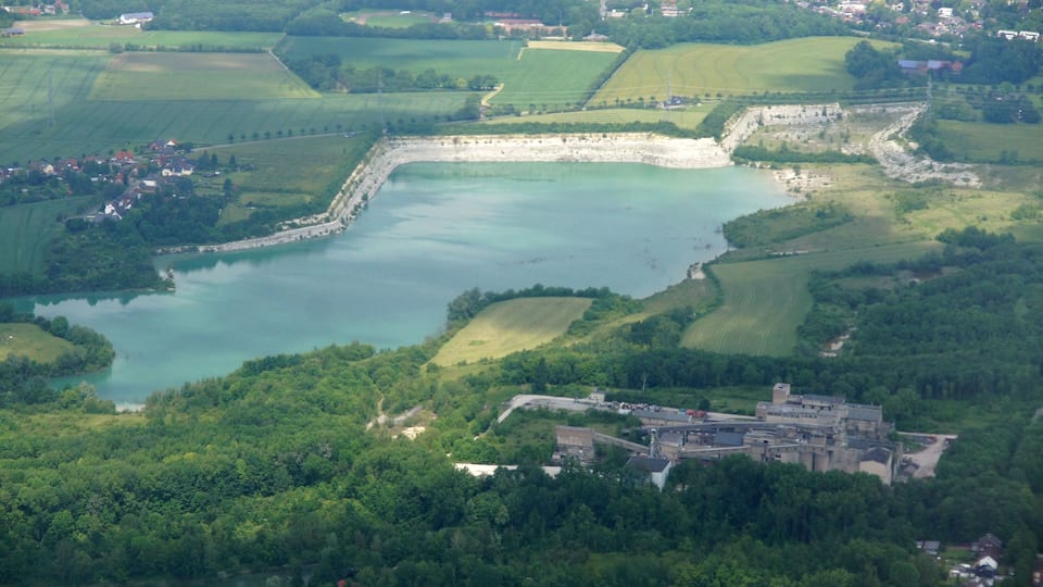 An aerial view of a lake surrounded by green fields and a castle-like structure.