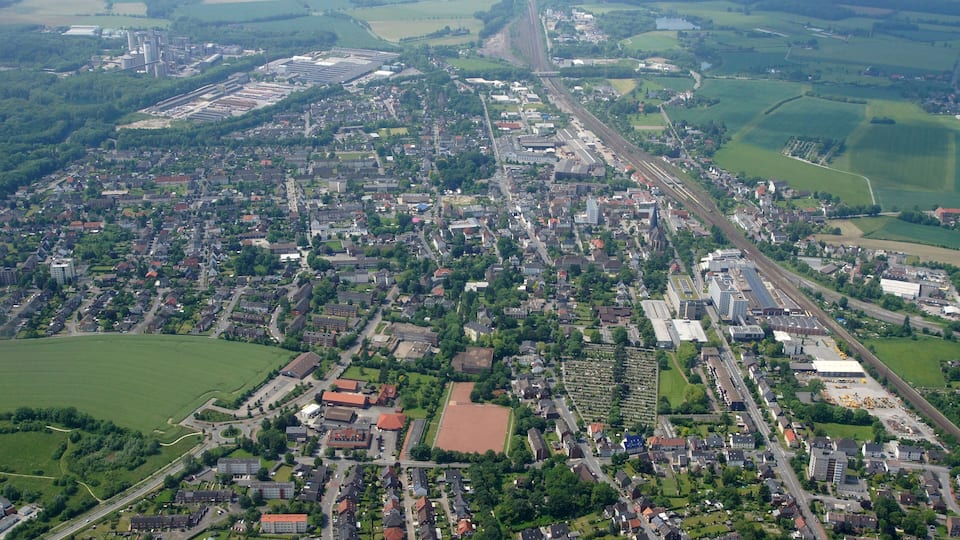 An aerial view of a town with a railway line, green fields, and residential areas.