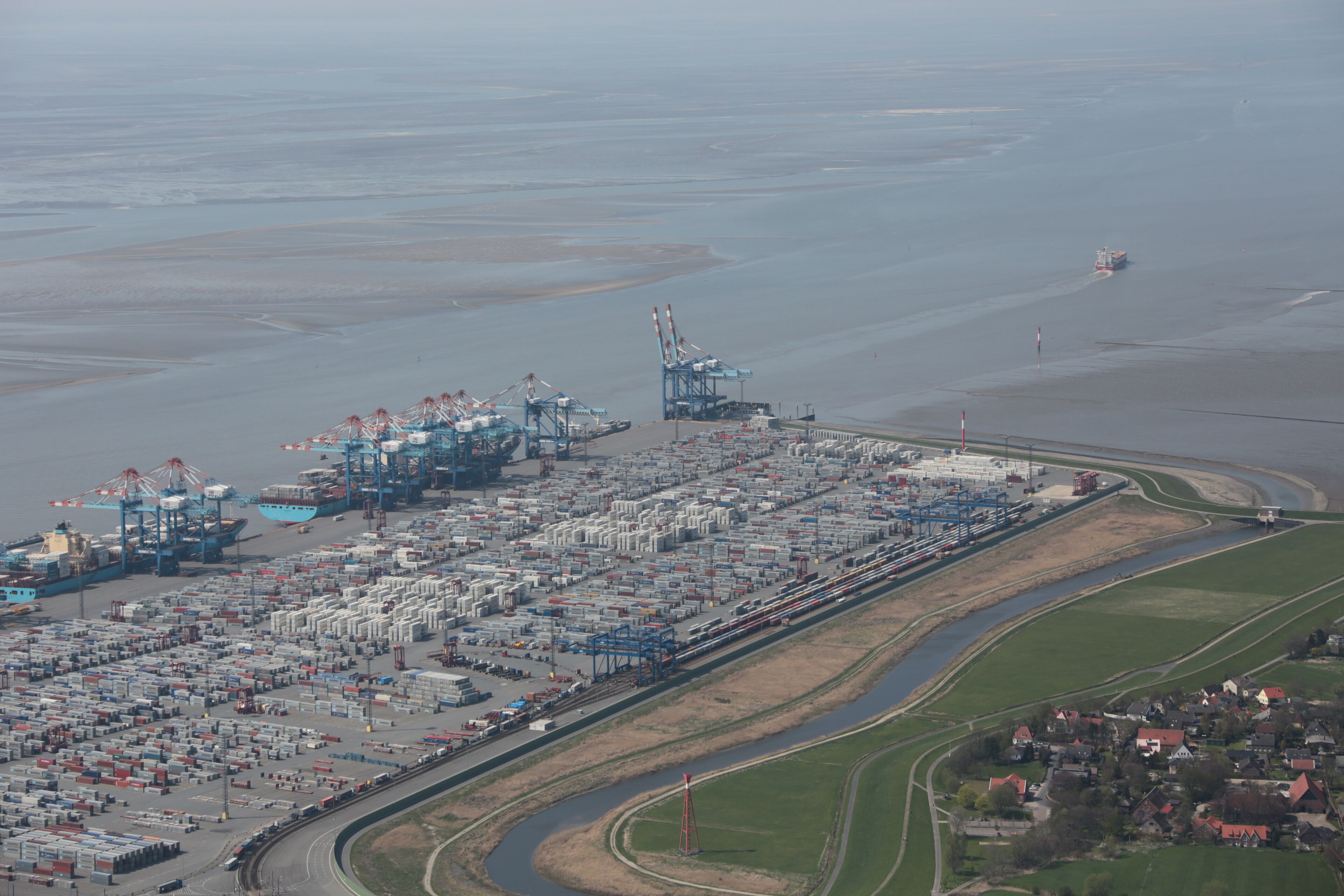 An industrial port with shipping containers, cranes, and a railway line.