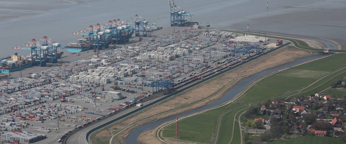 An industrial port with shipping containers, cranes, and a railway line.