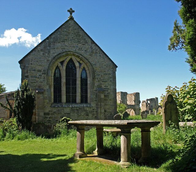 A stone church with a pointed roof and arched windows, surrounded by a cemetery with headstones.