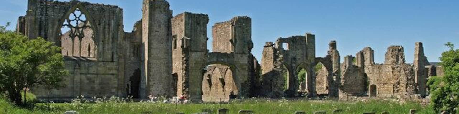 Ruina histórica con muros de piedra y un amplio ventanal de arco, rodeada por un cementerio con lápidas.