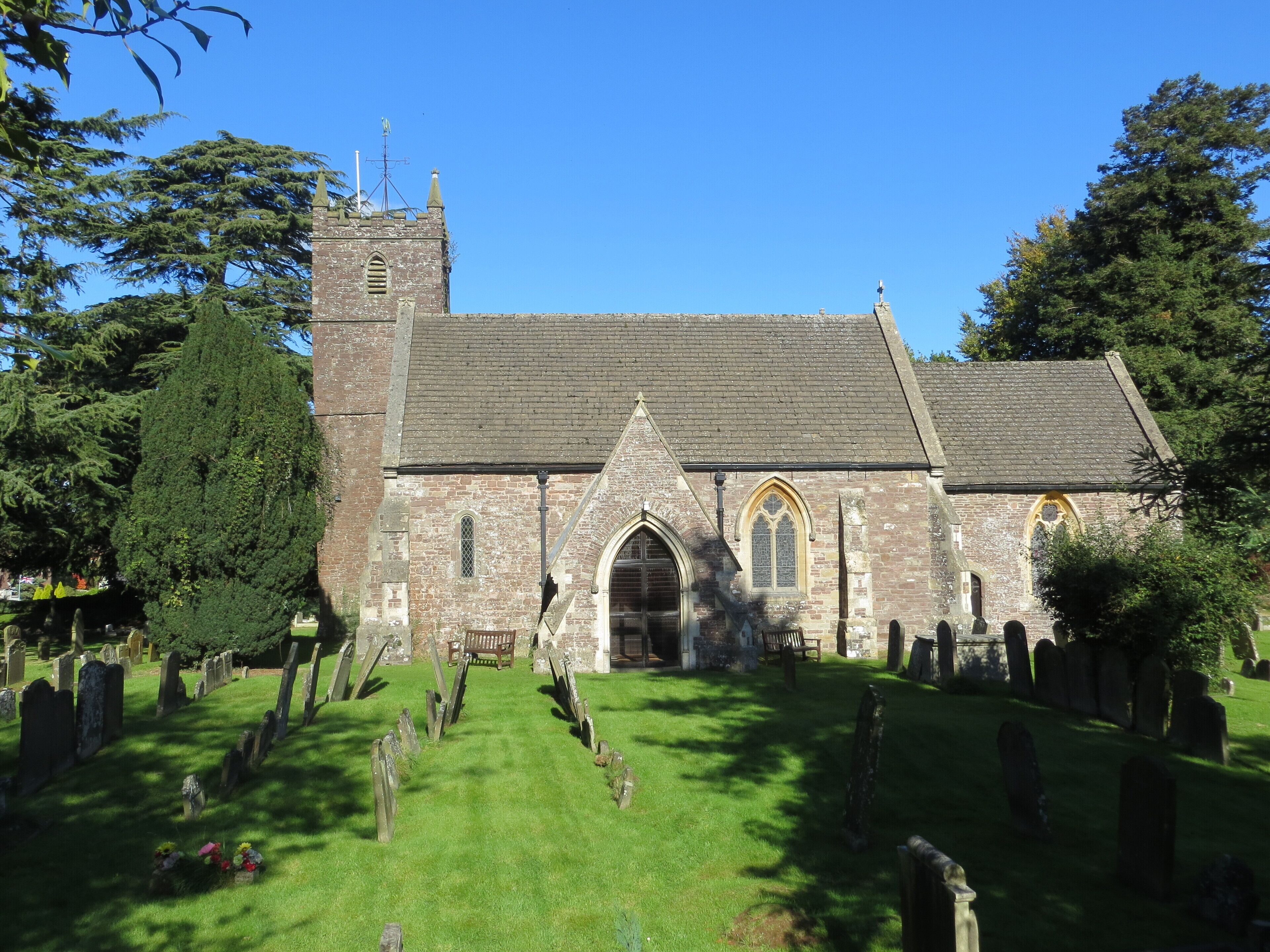 A church with a tall tower, arched windows, and a graveyard in front.