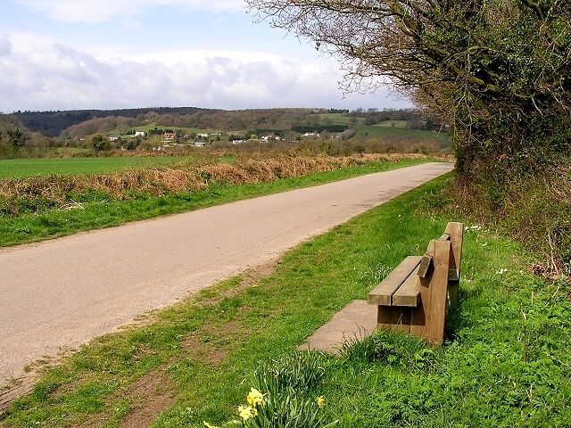 A rural road with a wooden bench on the side.