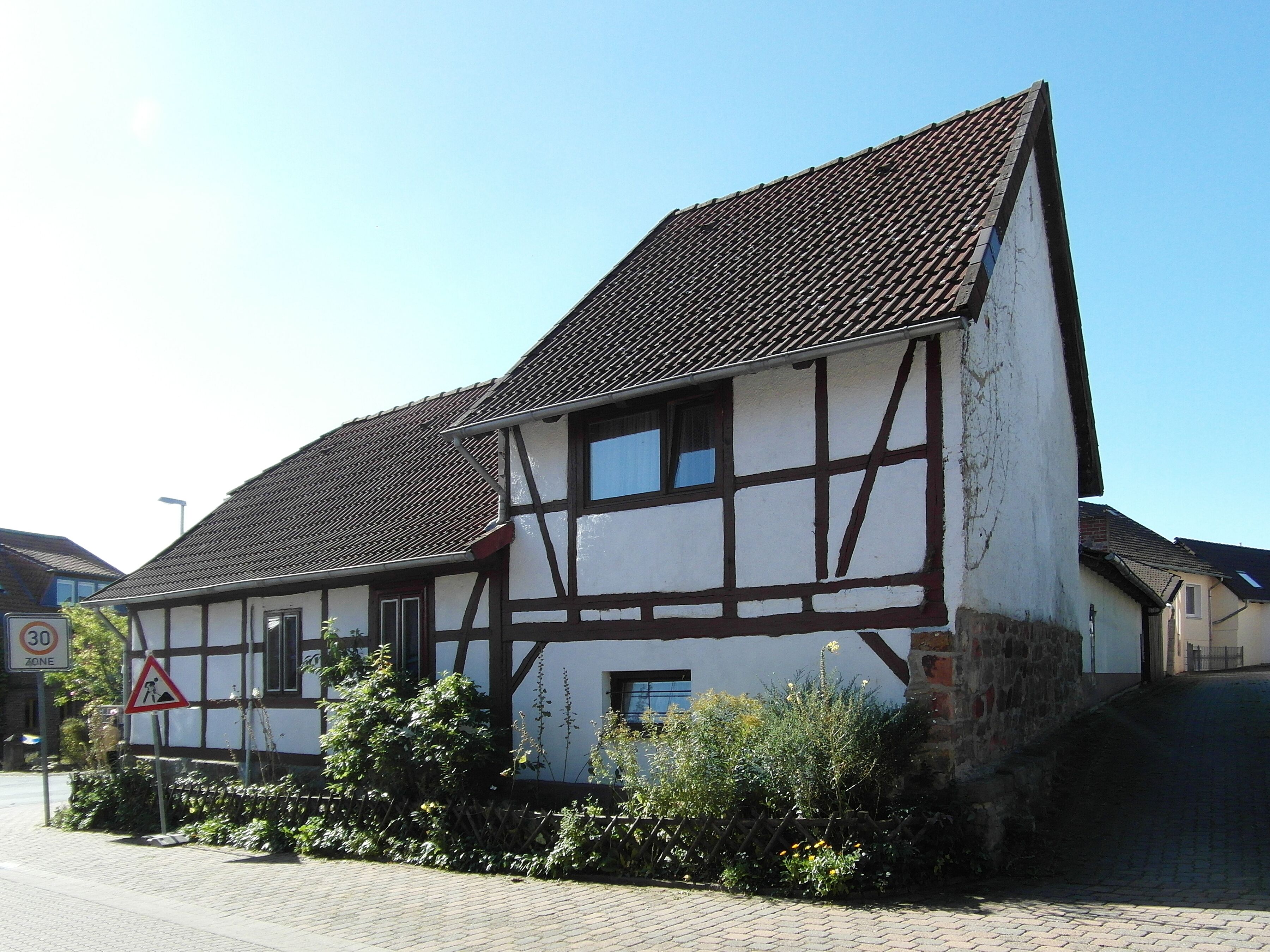 A traditional half-timbered house with a steeply pitched roof and a '30 zone' speed limit sign.