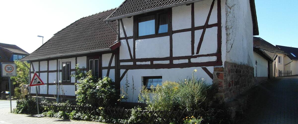A traditional half-timbered house with a steeply pitched roof and a '30 zone' speed limit sign.
