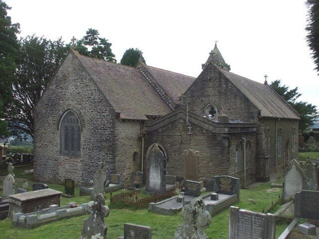 A small stone church with a pointed roof and arched windows, surrounded by a cemetery with headstones.