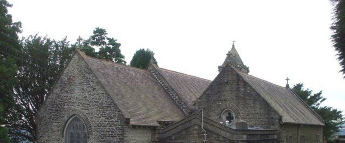 A small stone church with a pointed roof and arched windows, surrounded by a cemetery with headstones.